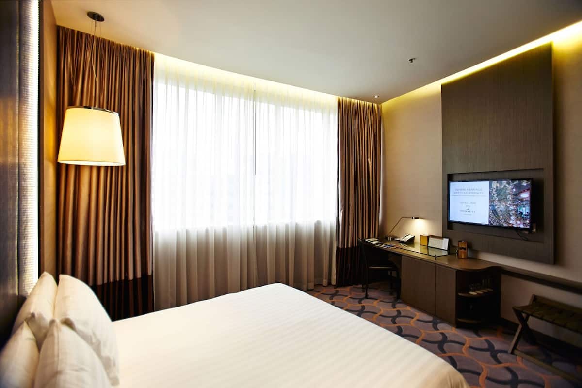 Ein Hotelzimmer mit einem Bett, einem Schreibtisch mit Lampe, einem Fernseher und Vorhängen.