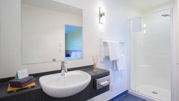 Une salle de bain moderne avec un lavabo blanc, une douche en verre et un grand miroir.