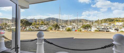 A view from a balcony with a rope barrier, a table, and chairs, overlooking a marina with boats and hills in the background.