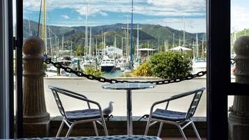 A view from a balcony with two chairs and a table, overlooking a marina with boats and a mountainous backdrop.