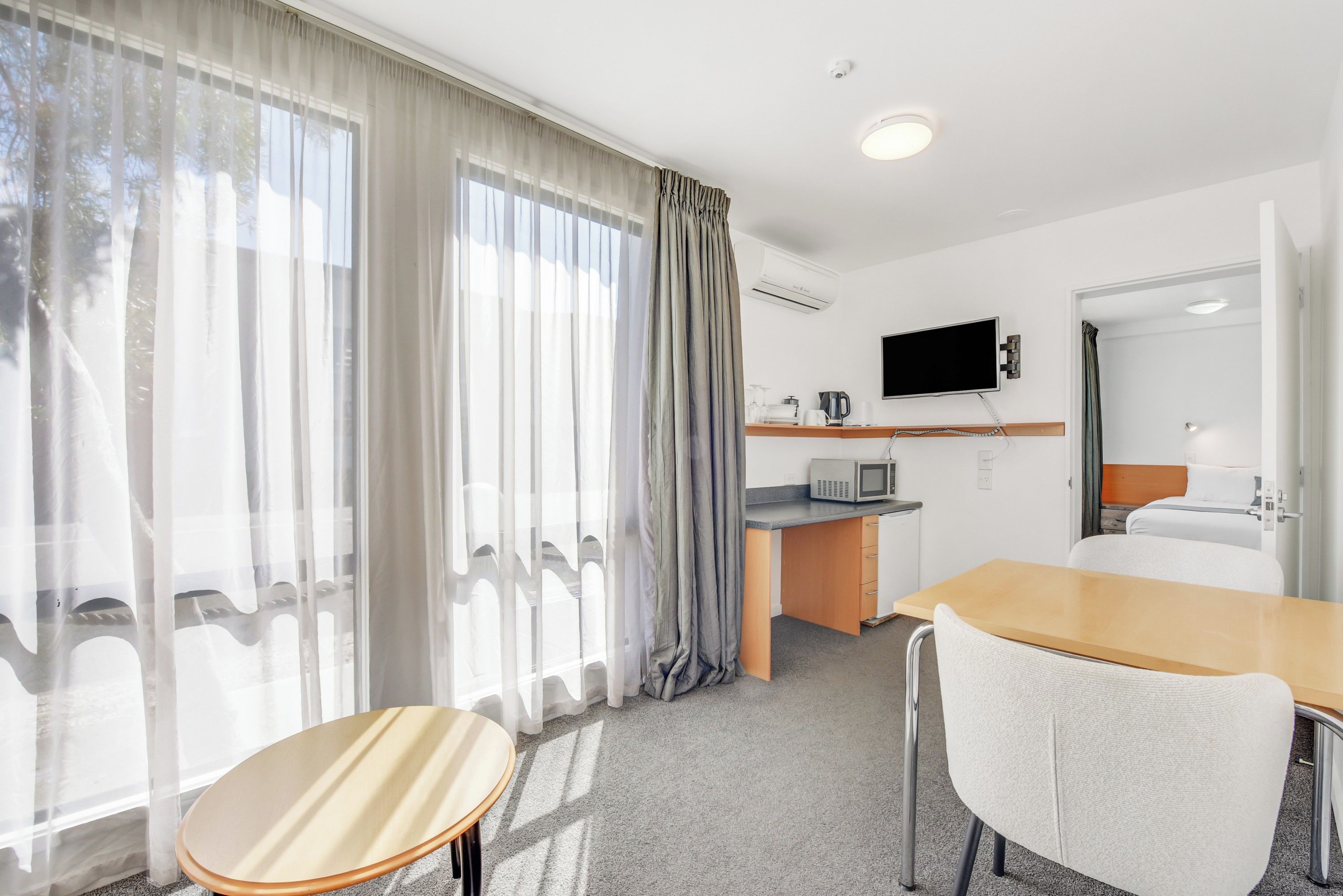 A hotel room with a dining area, a bed, a TV, and a kitchenette.