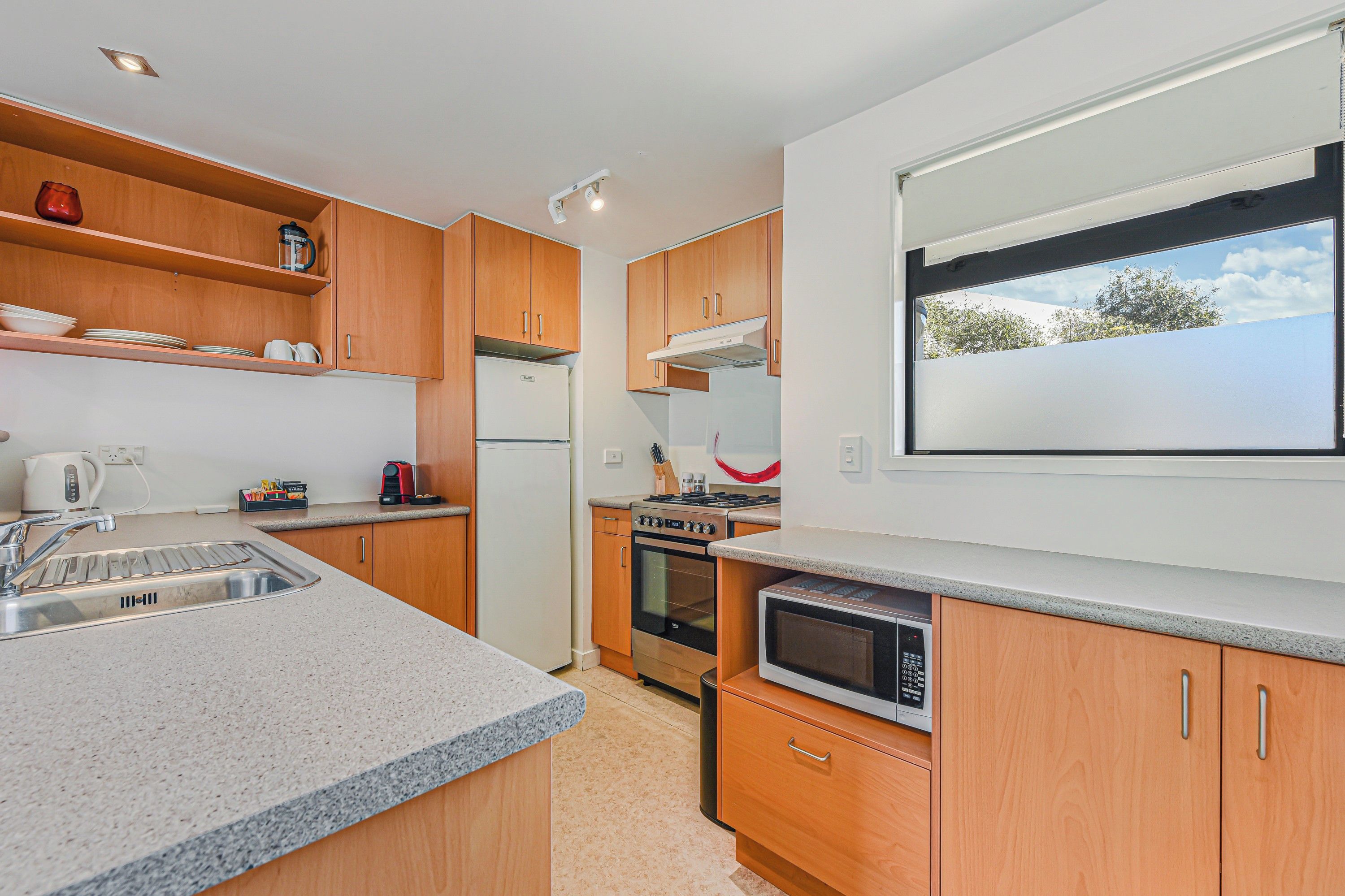 Cocina moderna con encimeras de granito, armarios de madera, horno empotrado y ventana con vistas.