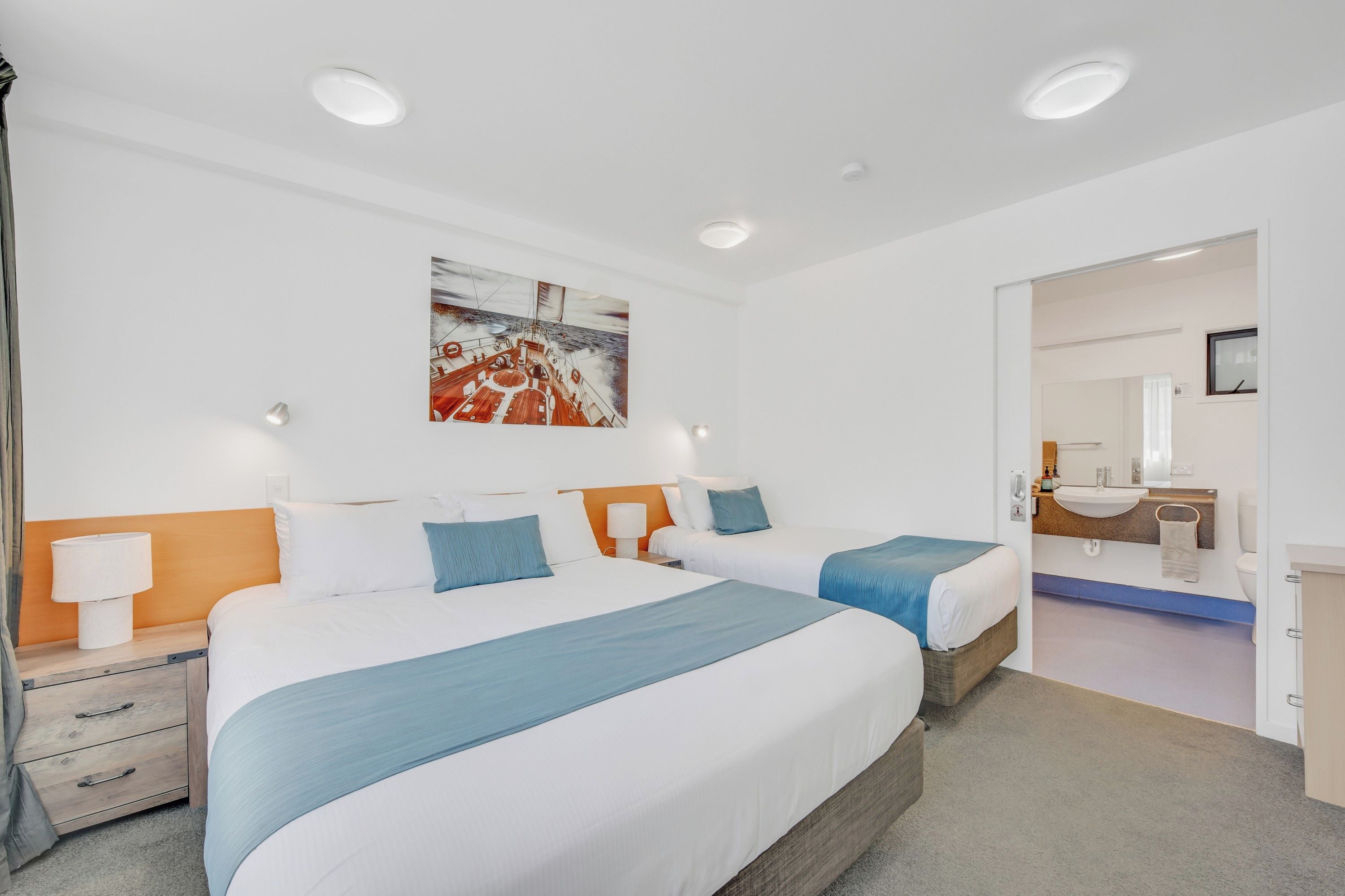 A hotel room with two beds, a painting on the wall, and a bathroom visible through an open door.