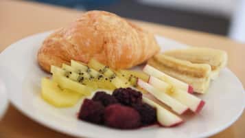 A plate with a croissant, sliced bananas, kiwi, apple, and berries.