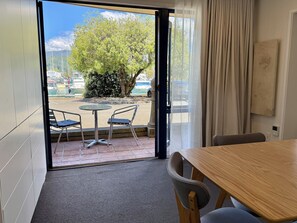A room with a wooden table and two chairs, a view of a marina with boats, and a large tree outside.