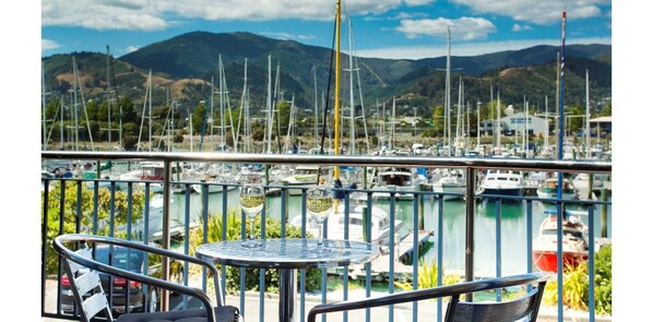 Un balcón con mesa y sillas que da a un puerto deportivo con numerosos barcos.