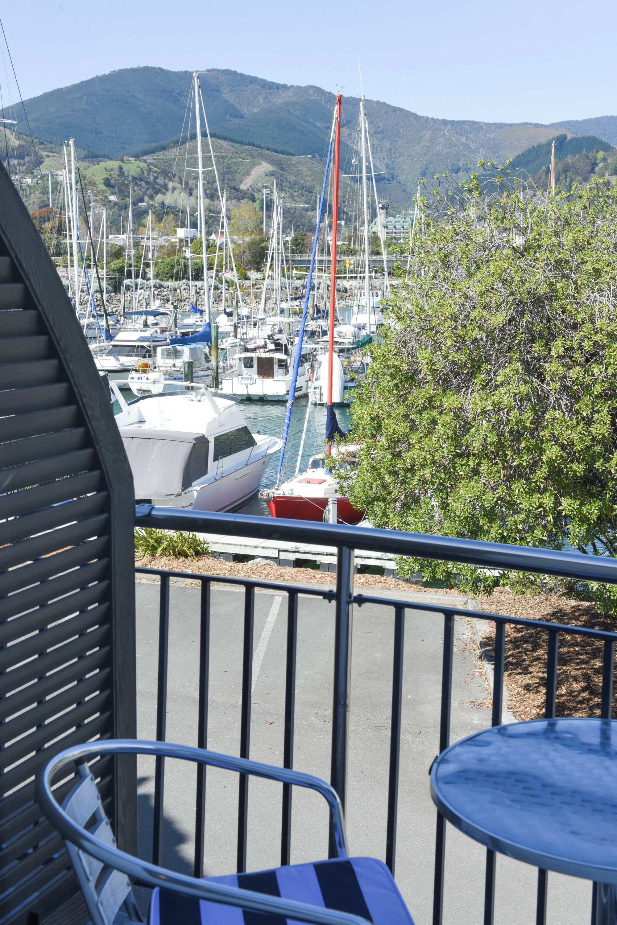 Marina com barcos atracados, vista das colinas ao redor e uma mesa e cadeira em primeiro plano.