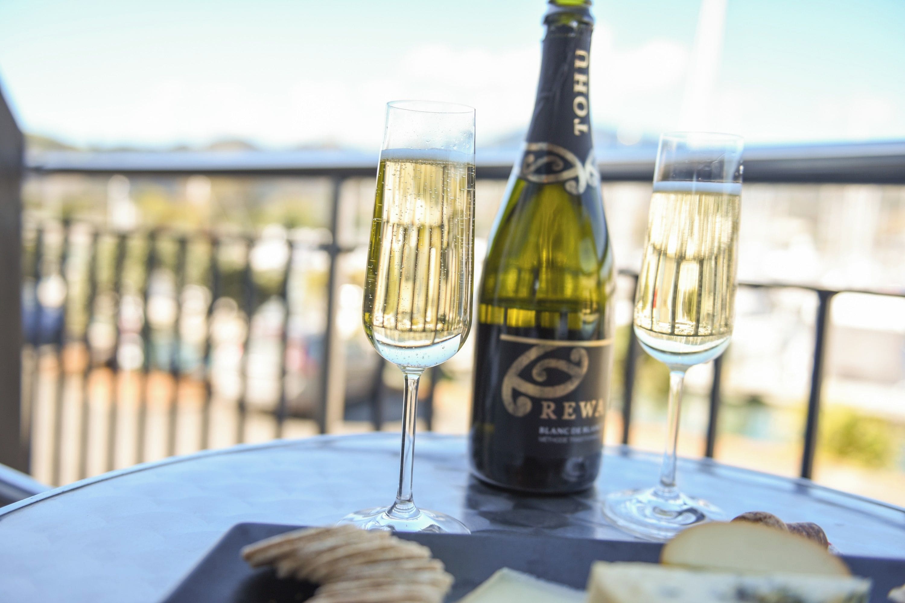 A bottle of champagne and two glasses on a table with a view of the outdoors.