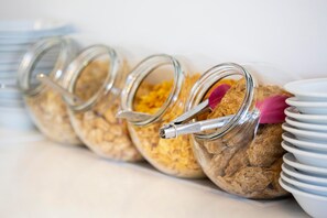 A row of glass jars with metal lids, each containing a brown substance and a pink object, placed on a white surface with stacked white plates beside them.