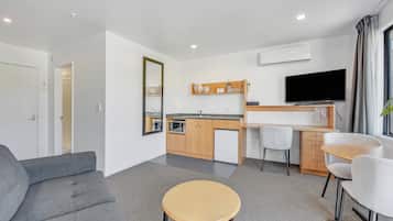 Uma sala de estar moderna com um sofá cinzento, uma mesa de centro redonda de madeira e uma TV fixada na parede.