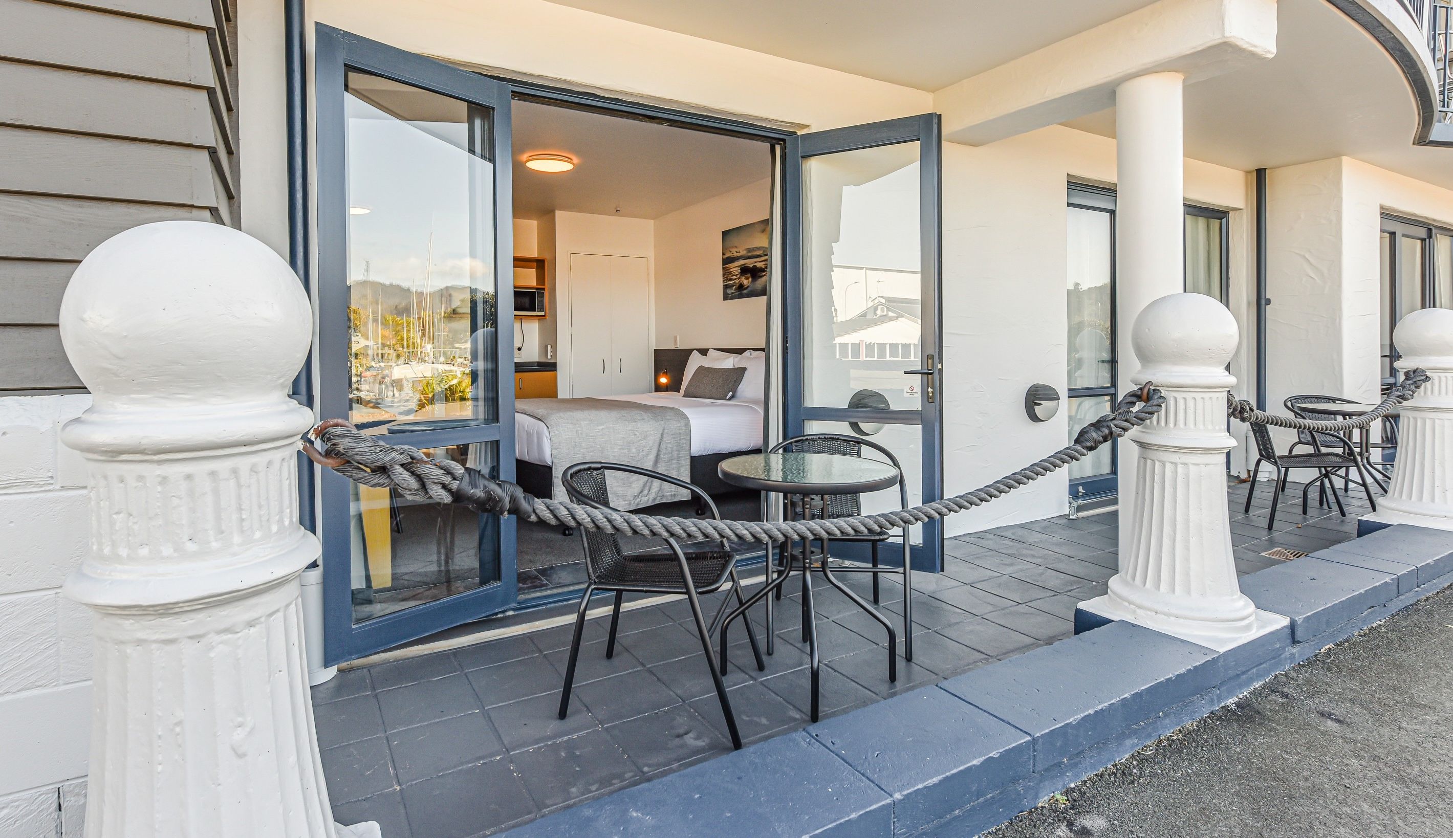 Une chambre d’hôtel avec un lit, une petite table et une chaise. Une barrière faite de cordes se trouve devant la porte de la chambre.