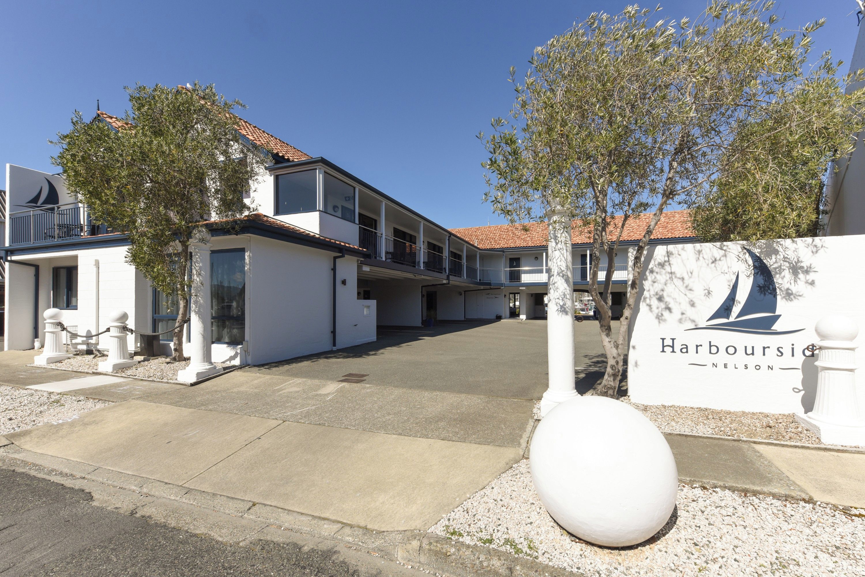 Un bâtiment blanc avec une enseigne indiquant « Harbourside Nelson » et un grand objet sphérique blanc au premier plan.