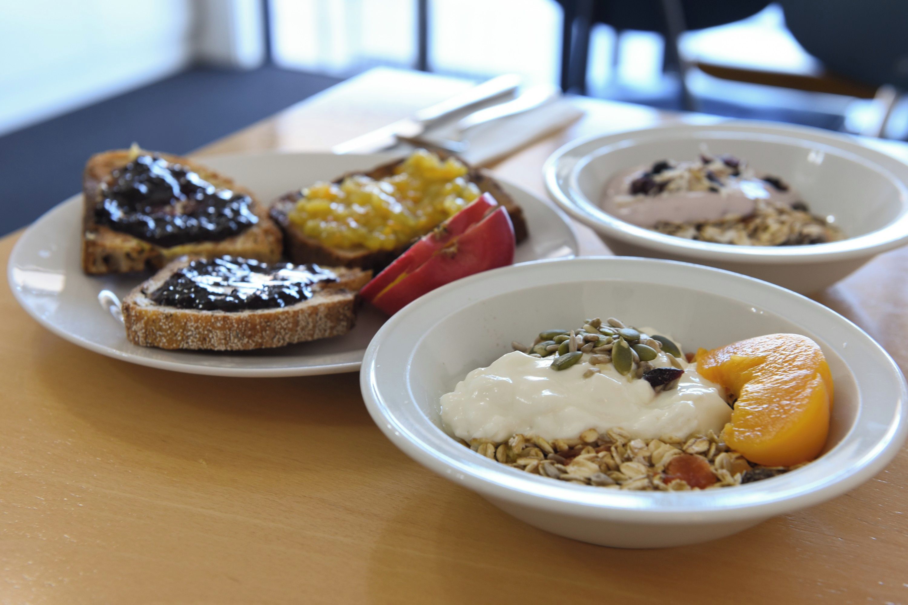 A breakfast setting with toast, fruit, yogurt, and granola on a wooden table.