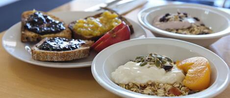 A breakfast setting with toast, fruit, yogurt, and granola on a wooden table.