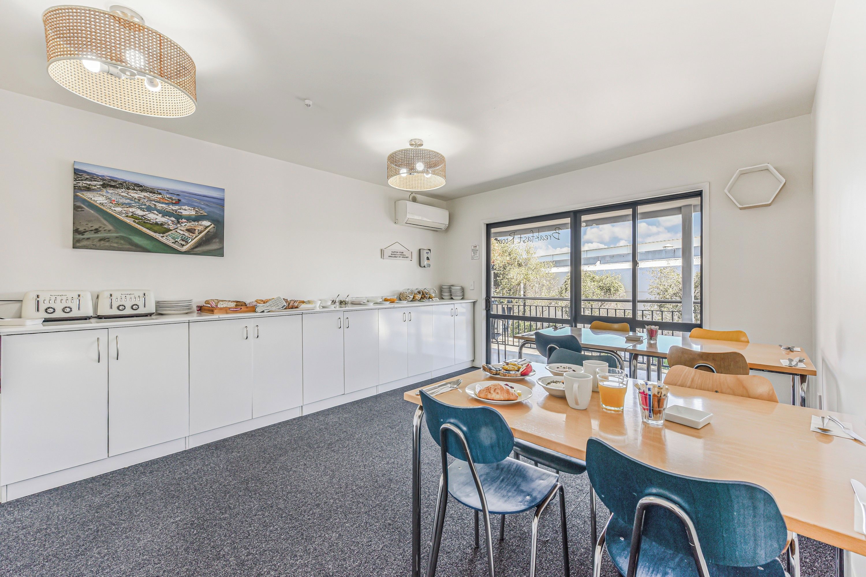A modern kitchen with white cabinets, a dining area with blue chairs, and a large window offering a view of the outdoors.