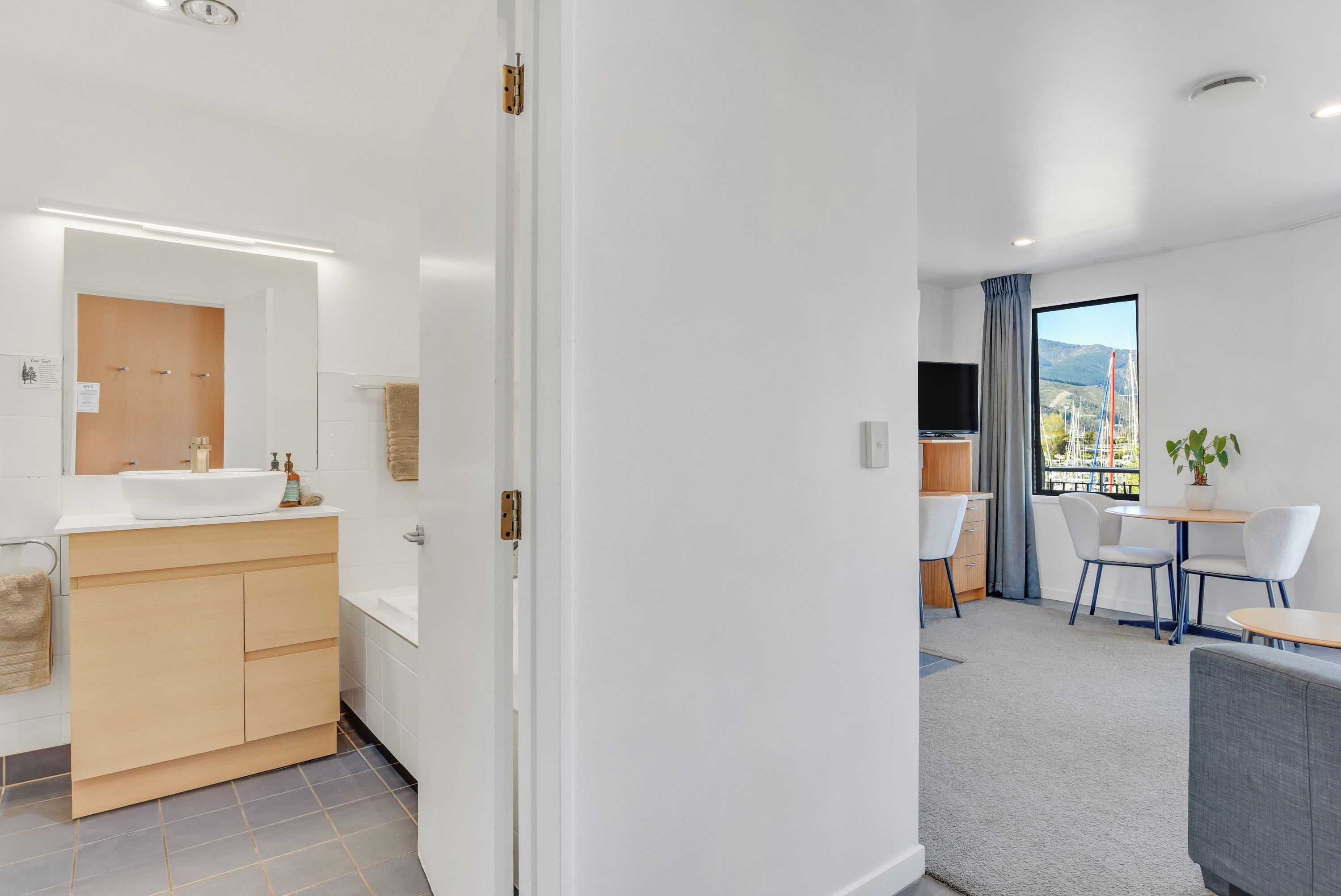 A modern hotel room with a bathroom, a dining area, and a view of the outdoors.