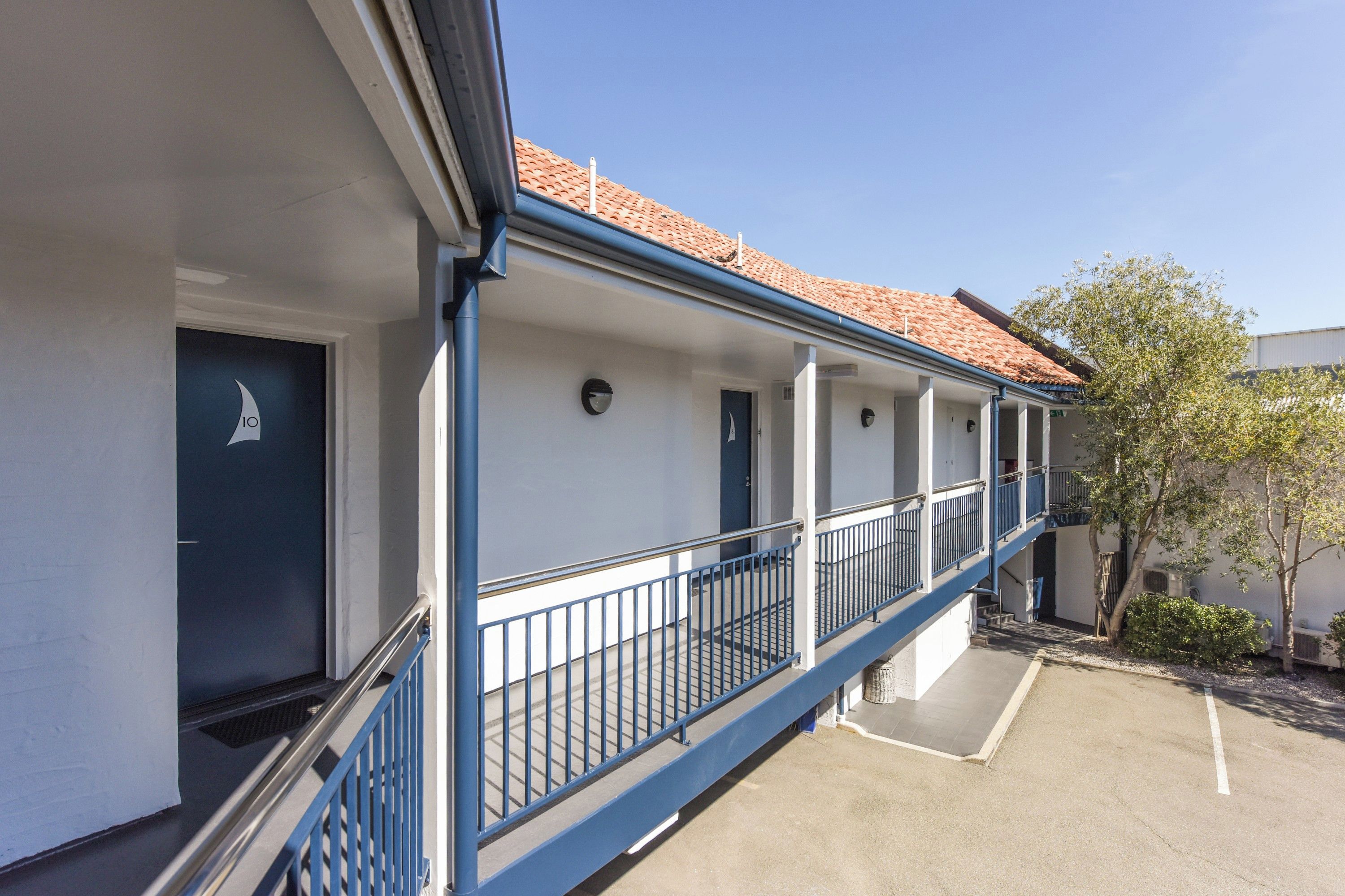 A building with a balcony, a door with a sailboat symbol, and a clear sky.