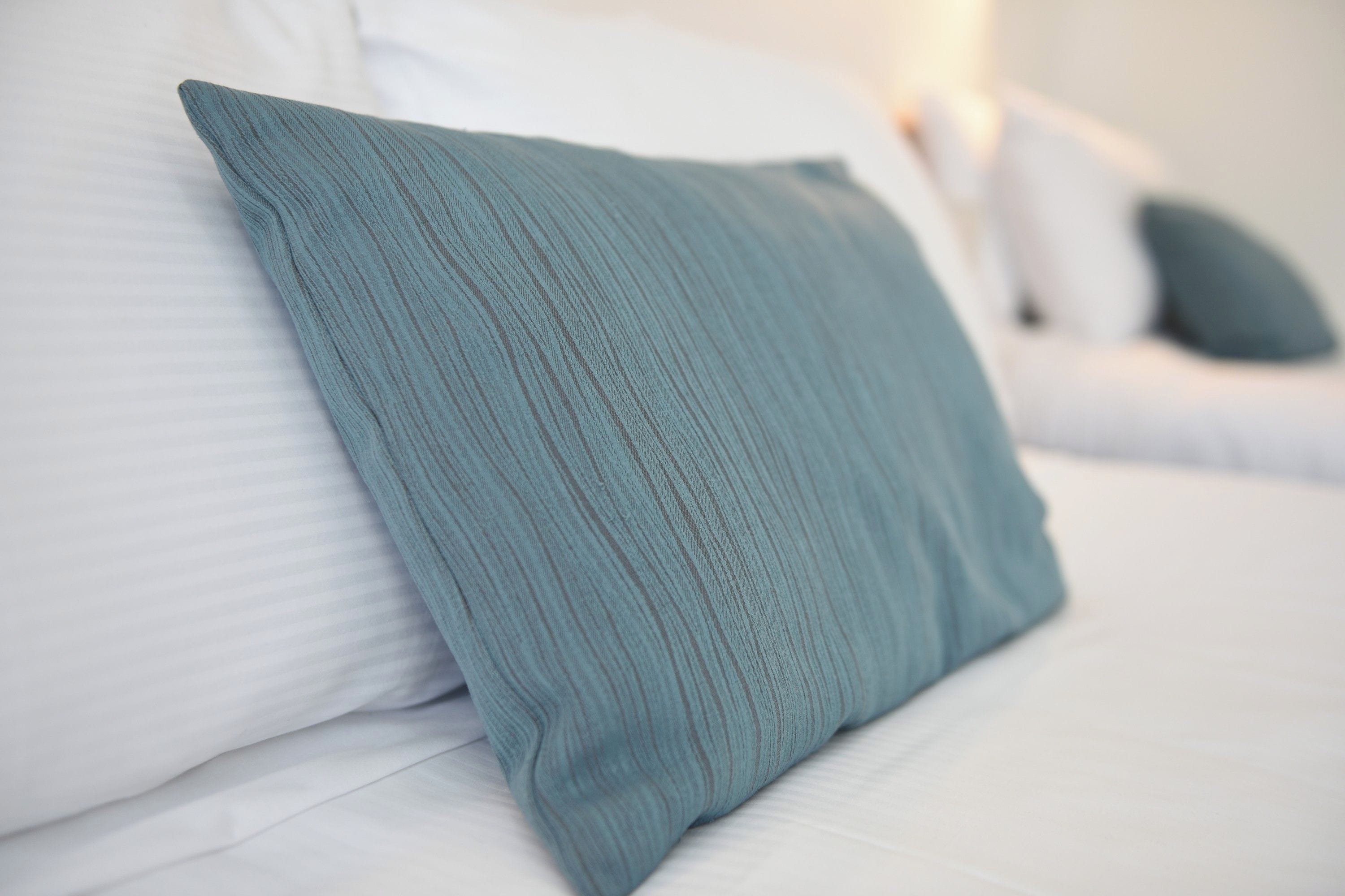 A bed with white bedding and a teal pillow.