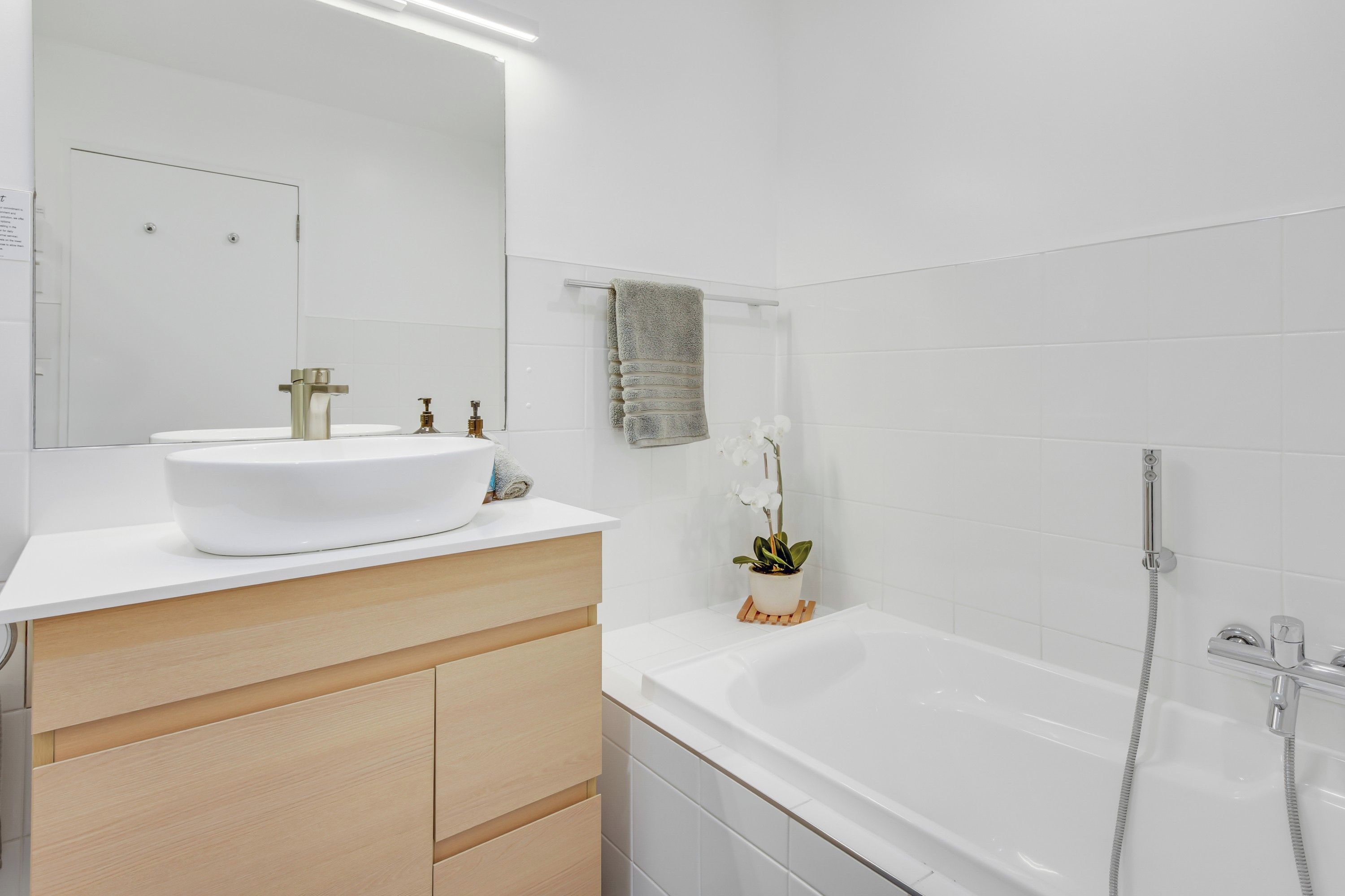 A modern bathroom with a white sink, mirror, and a shower with a handheld showerhead.