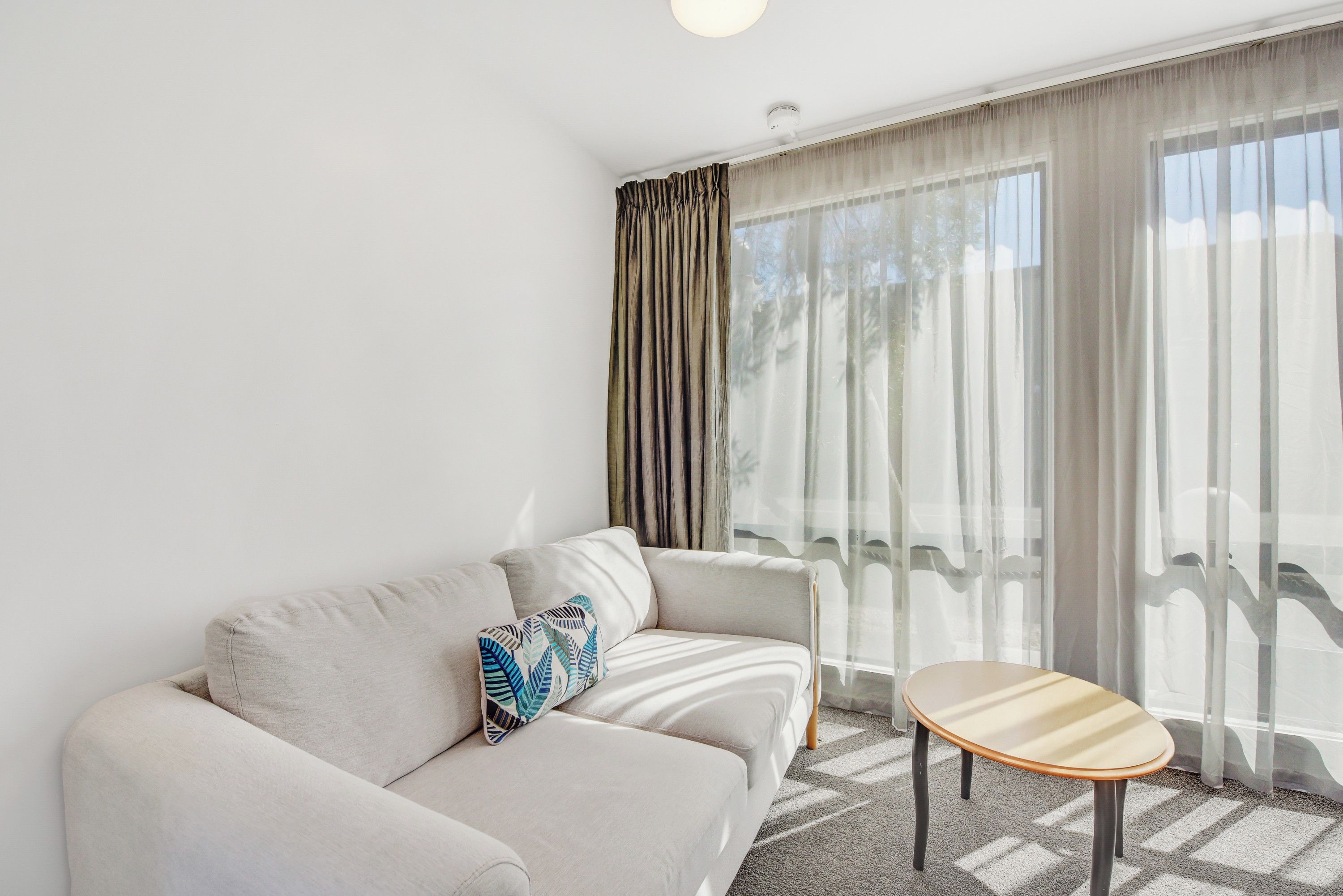 En moderne stue med sofa, et rundt bord og lette gardiner.