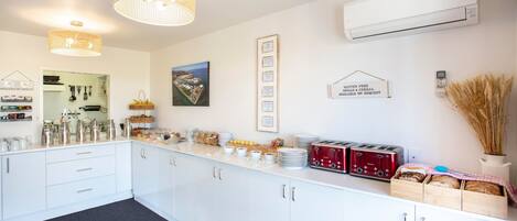 A modern kitchen with white cabinets, a countertop with various food items, a red toaster, and a hanging light fixture.
