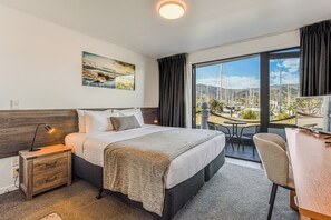 Ein Hotelzimmer mit Bett, Nachttisch, Schreibtisch und Blick auf eine Marina durch ein großes Fenster.