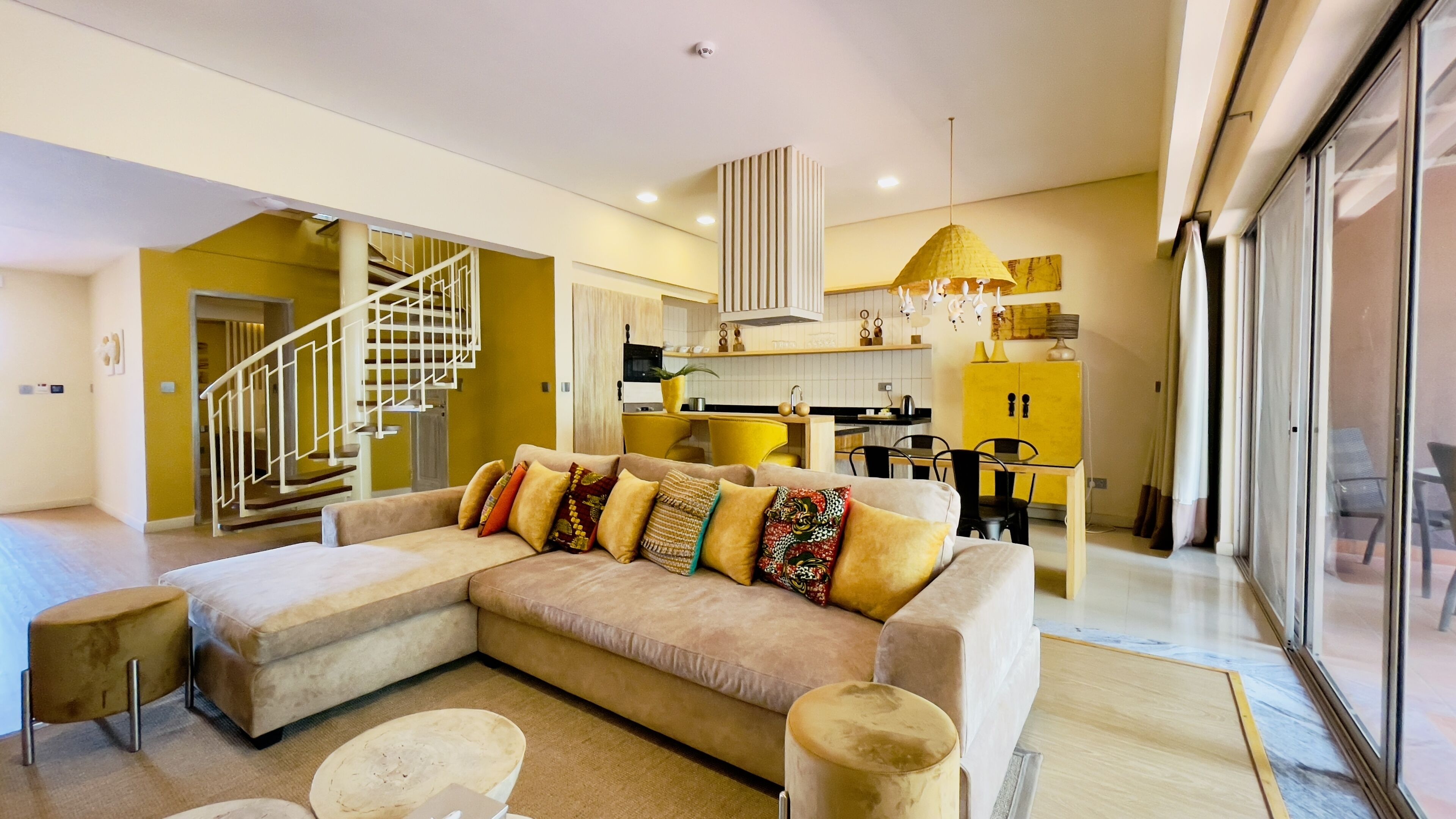 A modern living room with a large sectional sofa, a small round coffee table, and a staircase leading to an upper floor.