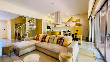 A modern living room with a large sectional sofa, a small round coffee table, and a staircase leading to an upper floor.