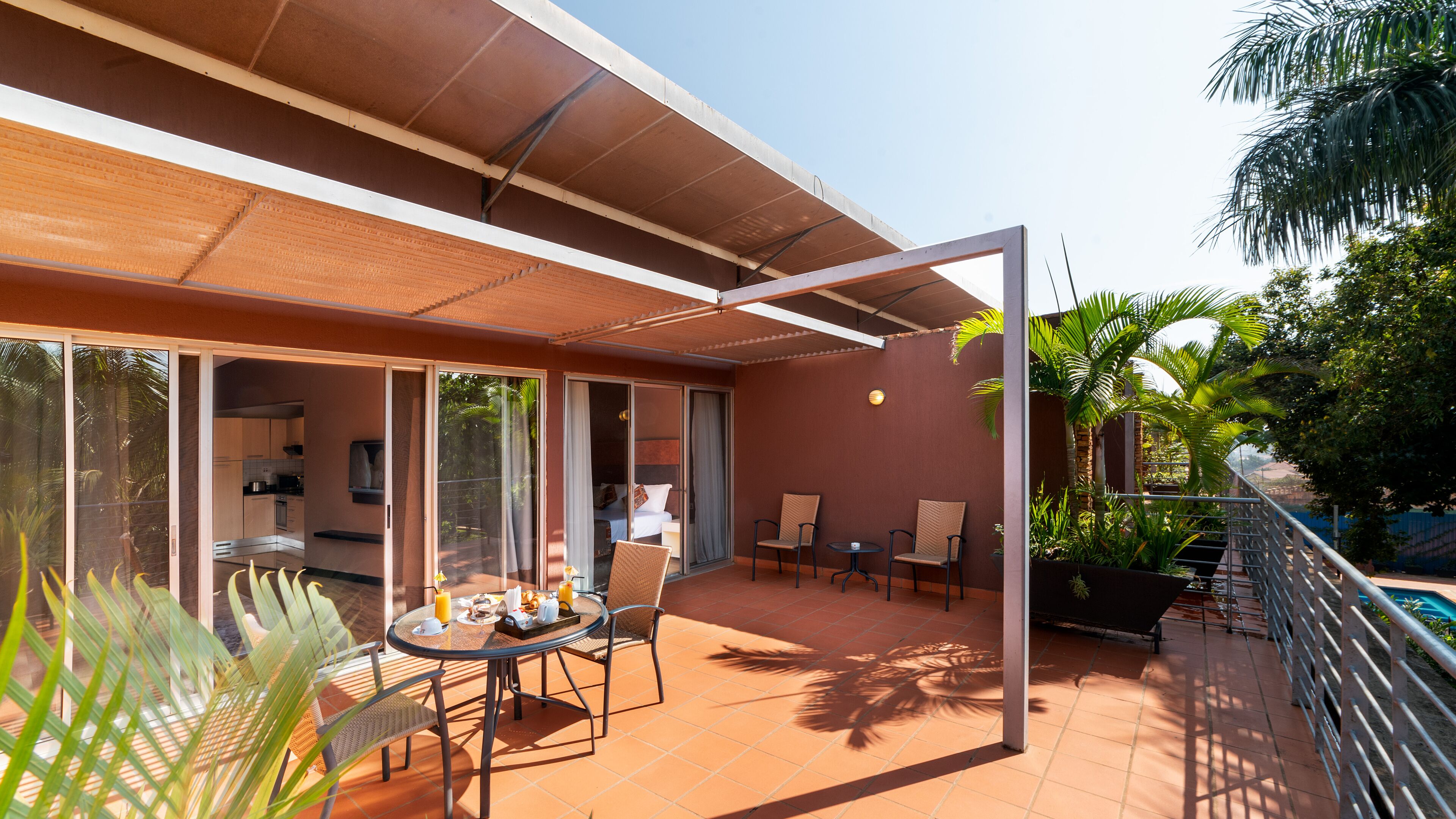 A modern outdoor patio with a dining table, chairs, and a kitchen area visible through large sliding doors.