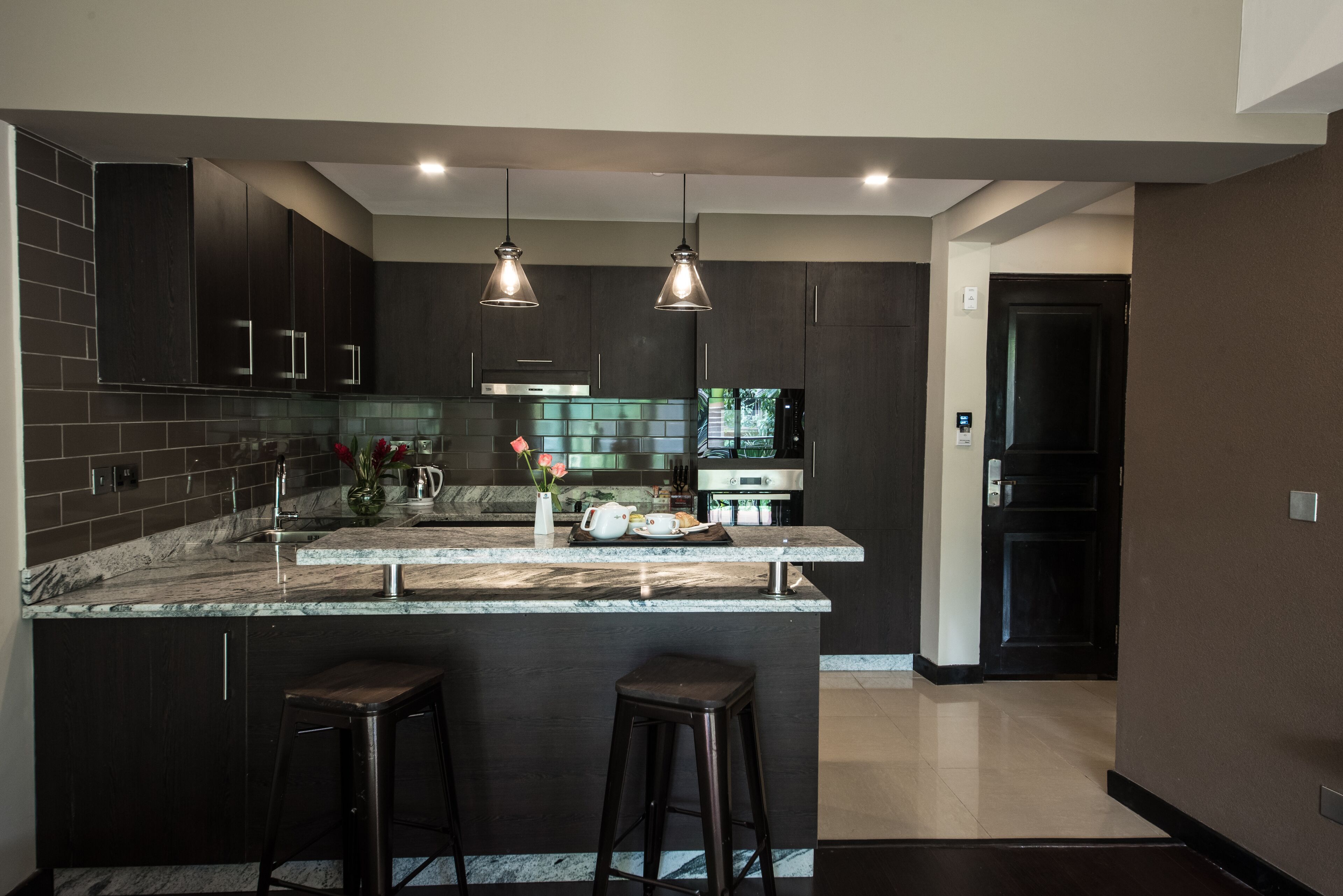 A modern kitchen with dark cabinetry, a marble countertop, and two bar stools.