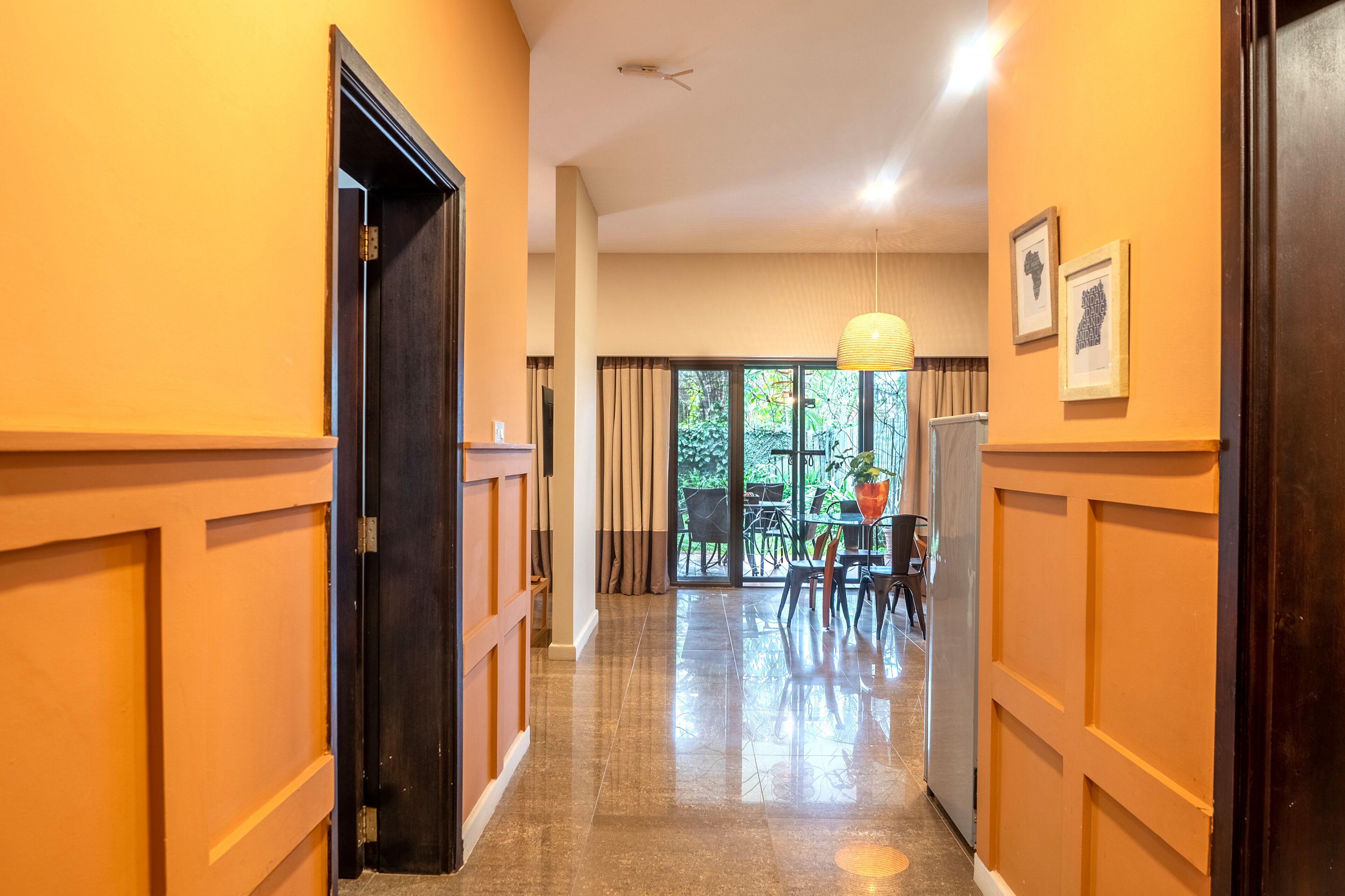 A hallway with a wooden door, a dining area with chairs and a table, and a large window with curtains.