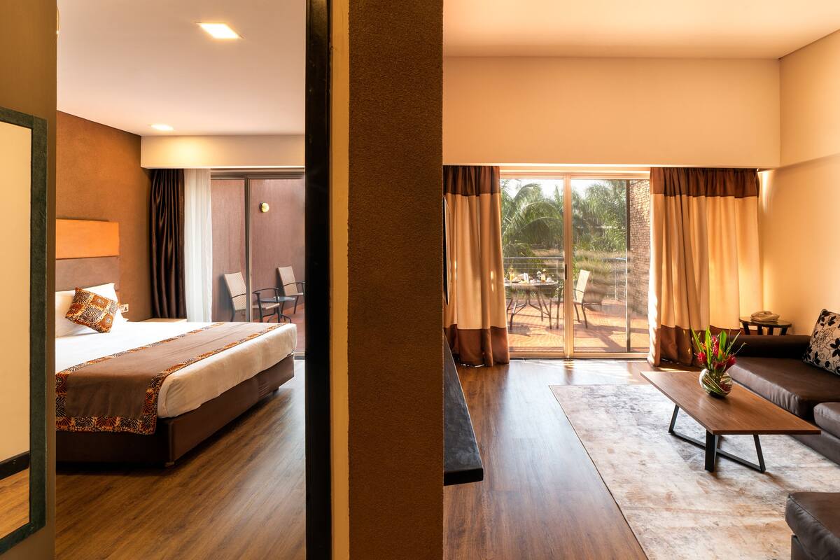 A hotel room with a bed, a sofa, a coffee table, and a view of the outdoors.