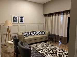 Un salon comprenant un canapé, un fauteuil, une lampe, une petite table et un tapis à motifs.