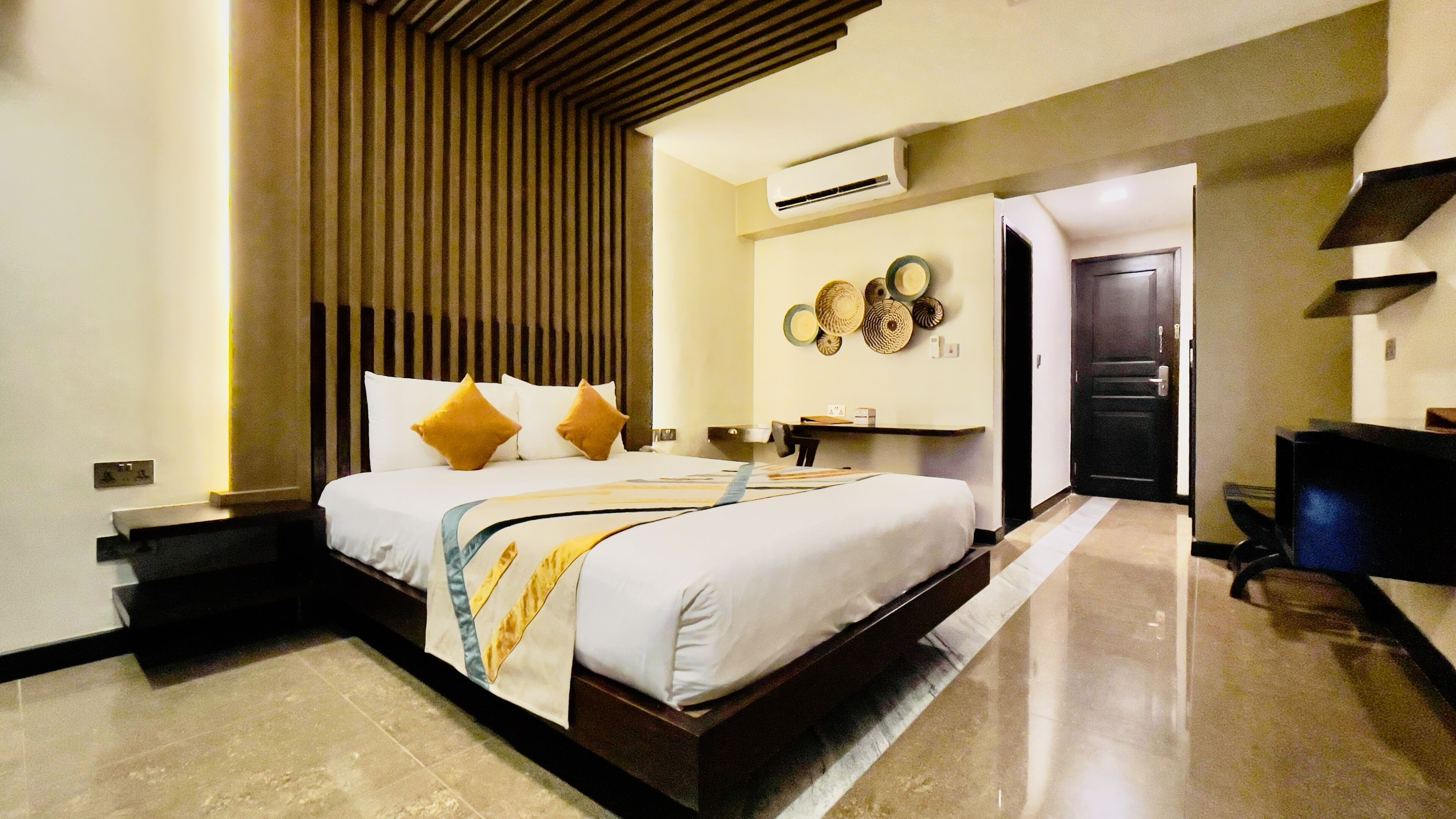 A modern hotel room with a large bed, a desk, and an air conditioning unit on the wall.