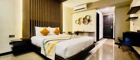 A modern hotel room with a large bed, a desk, and an air conditioning unit on the wall.