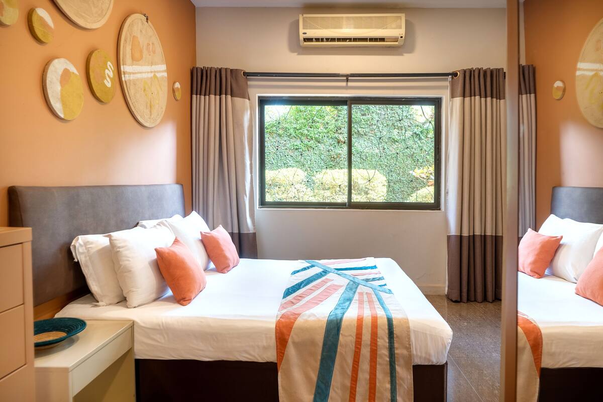 A hotel room with a bed, a dresser, a window with curtains, and wall art.