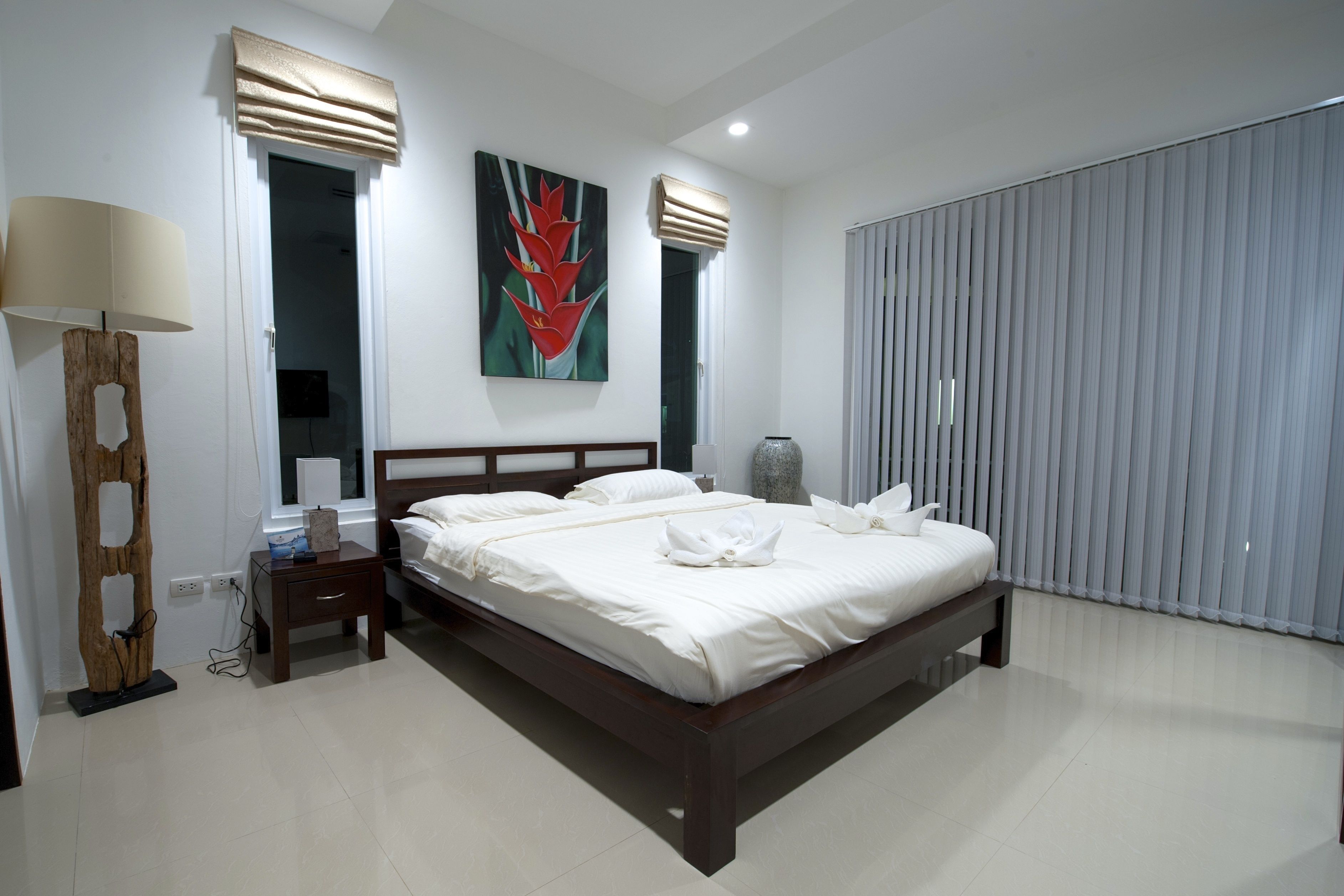 A modern bedroom with a large bed, a bedside table, a lamp, and a painting on the wall.