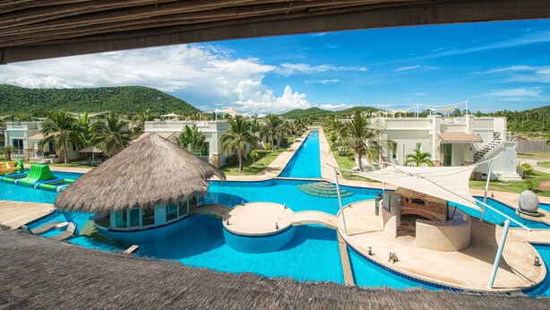 A resort with a large swimming pool, a thatched-roof structure, and a view of the mountains. - Oriental Beach Pearl Resort (Sam Roi Yot)