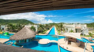 Relax by the multi-level pool with a water slide, surrounded by palm trees and lush green hills.