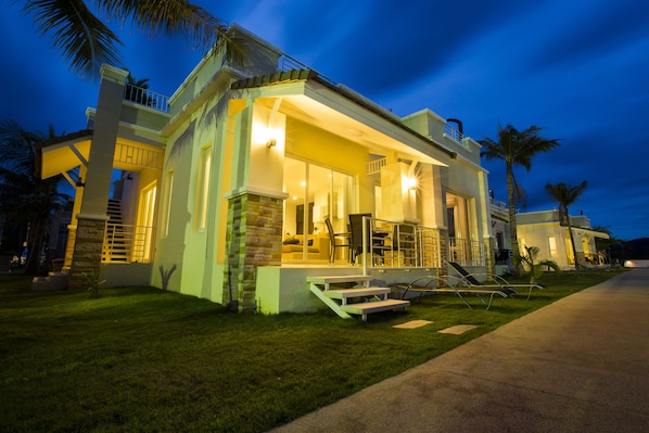 Una casa moderna con balcón, un patio con sillas y una entrada bien iluminada.