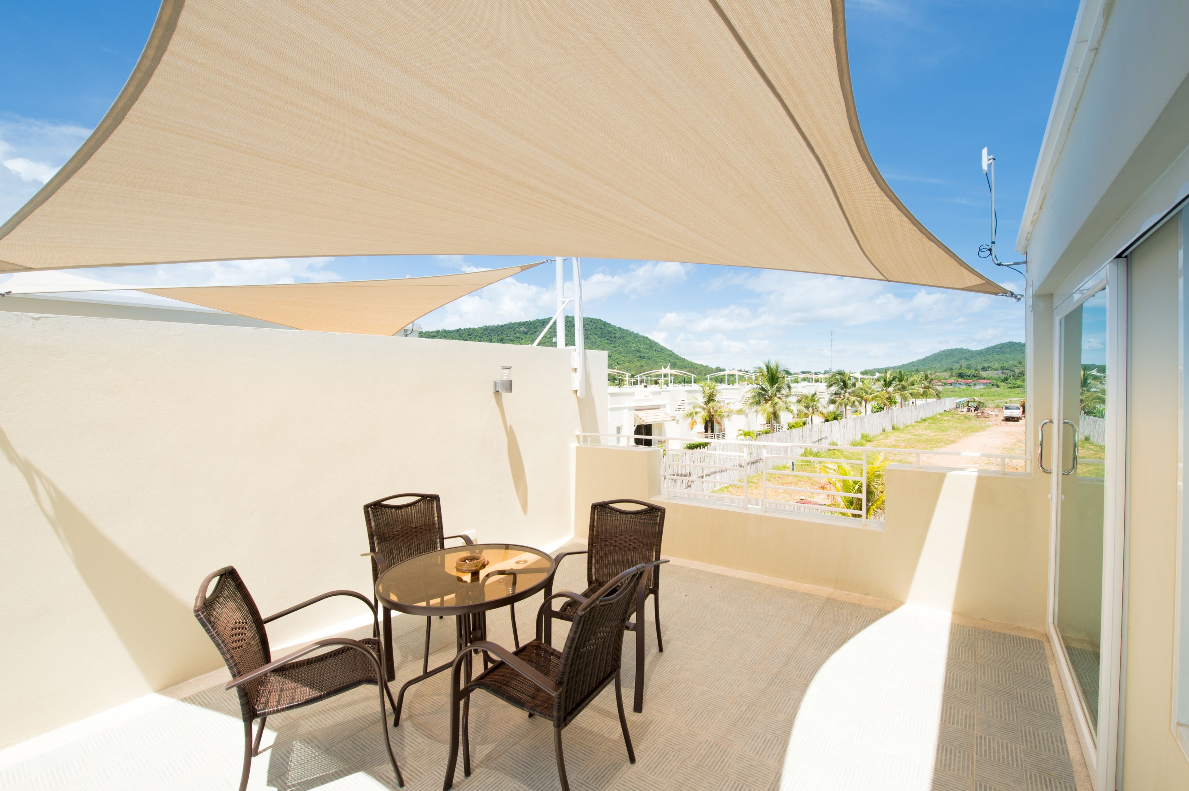 A balcony with a table and chairs, a large shade sail, and a view of a green landscape with hills.