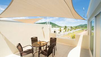 A balcony with a table and chairs, a large shade sail, and a view of a green landscape with hills.