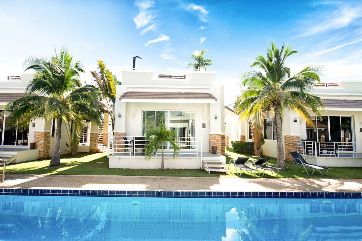 A modern hotel with a swimming pool, palm trees, and a clear blue sky.
