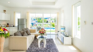 A modern living room with a sofa, coffee table, and a view of a swimming pool and garden. - Oriental Beach Pearl Resort (Sam Roi Yot)