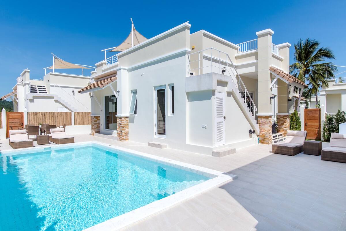 A modern villa with a swimming pool, outdoor seating, and a staircase leading to a balcony.