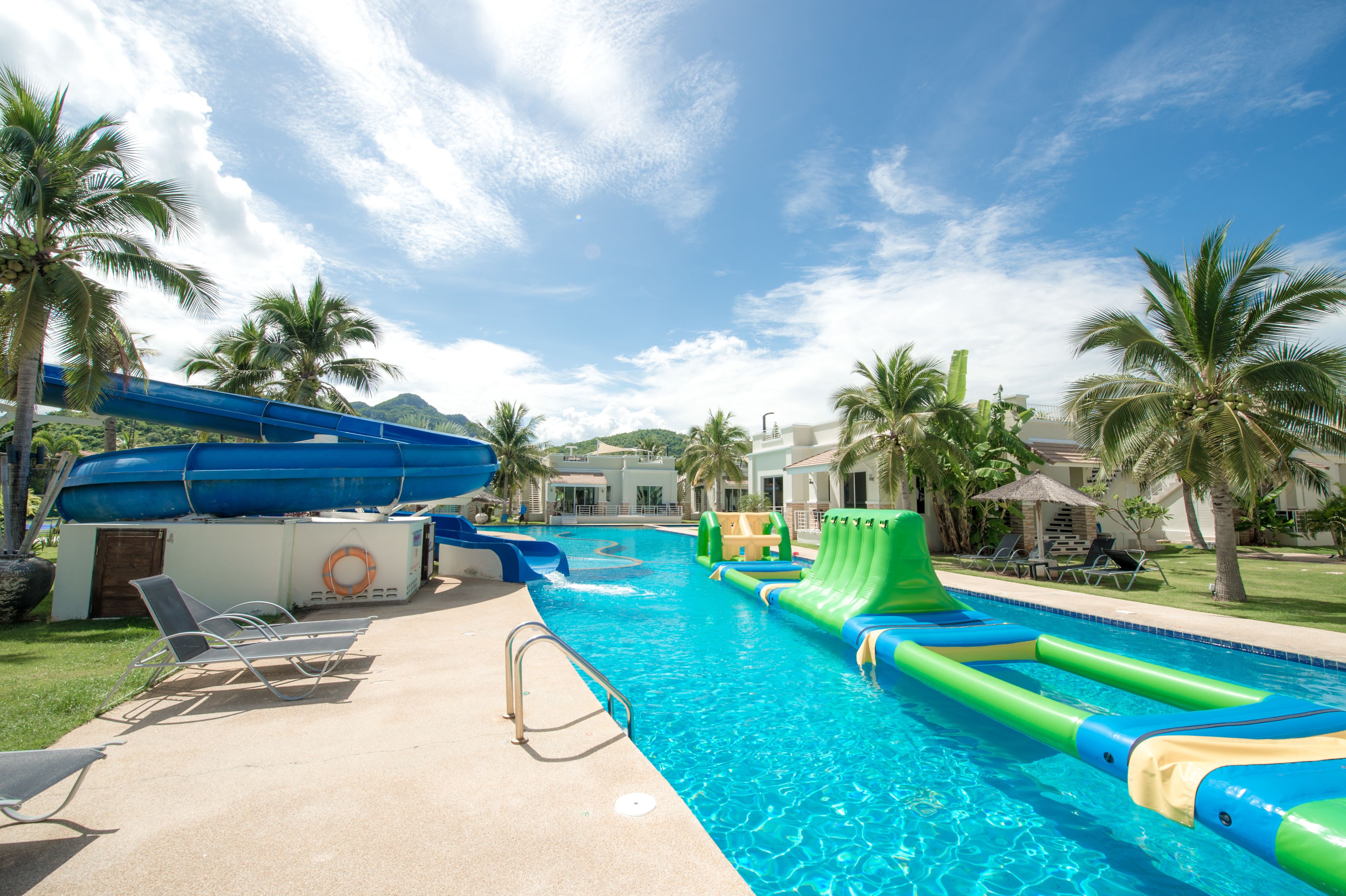 A swimming pool with slides and water toys, surrounded by palm trees and lounge chairs.