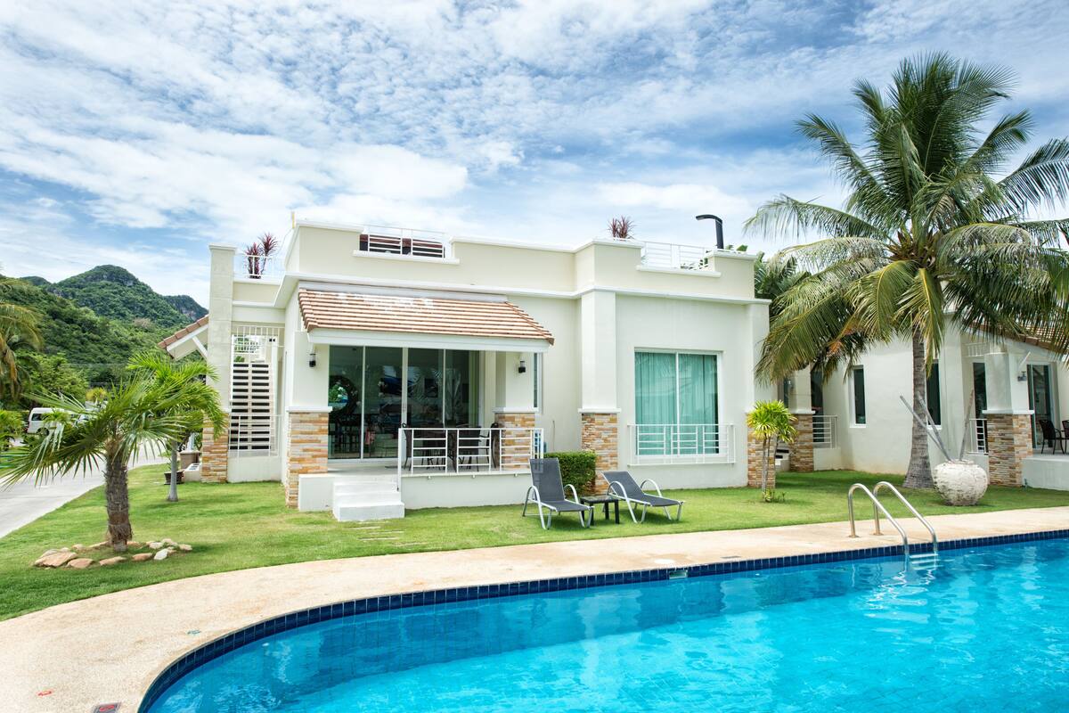 A modern house with a swimming pool, palm trees, and a mountain in the background.