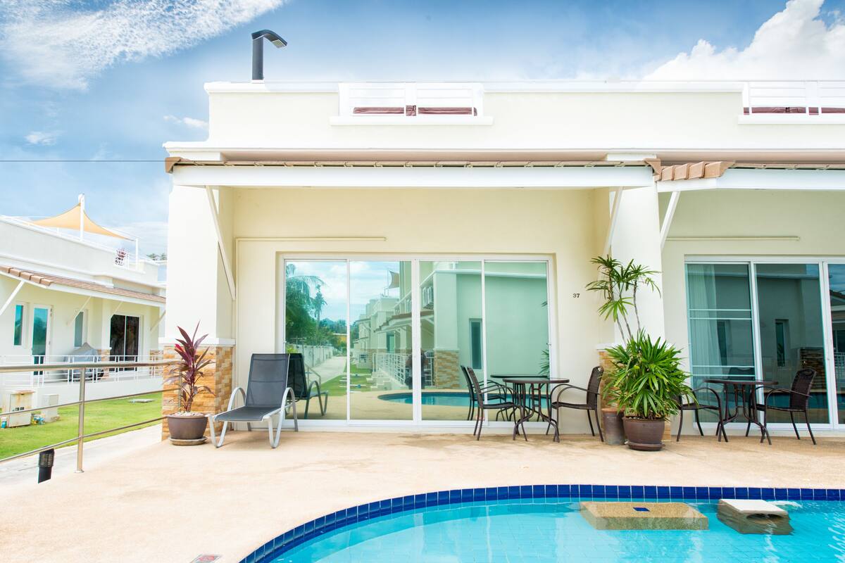 A modern building with a swimming pool, outdoor seating, and large windows.