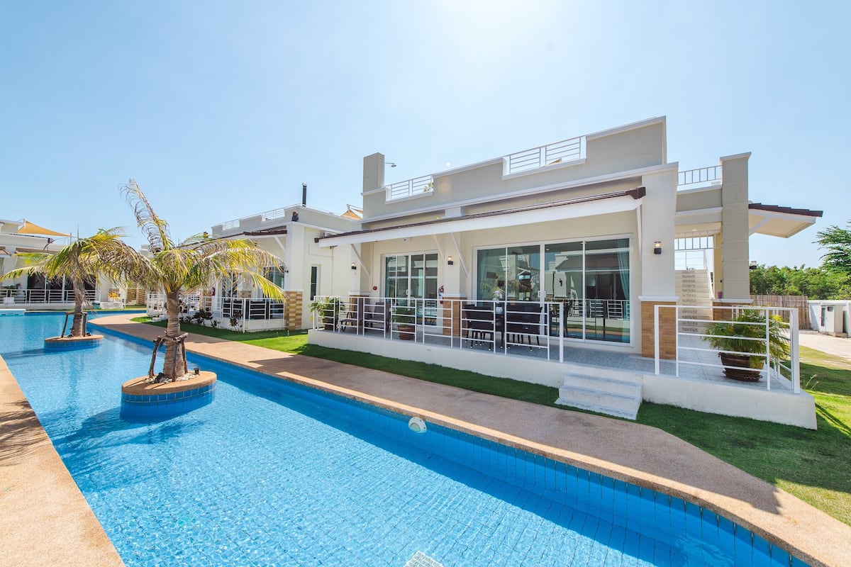 A modern hotel with a swimming pool, outdoor seating, and a well-maintained lawn.
