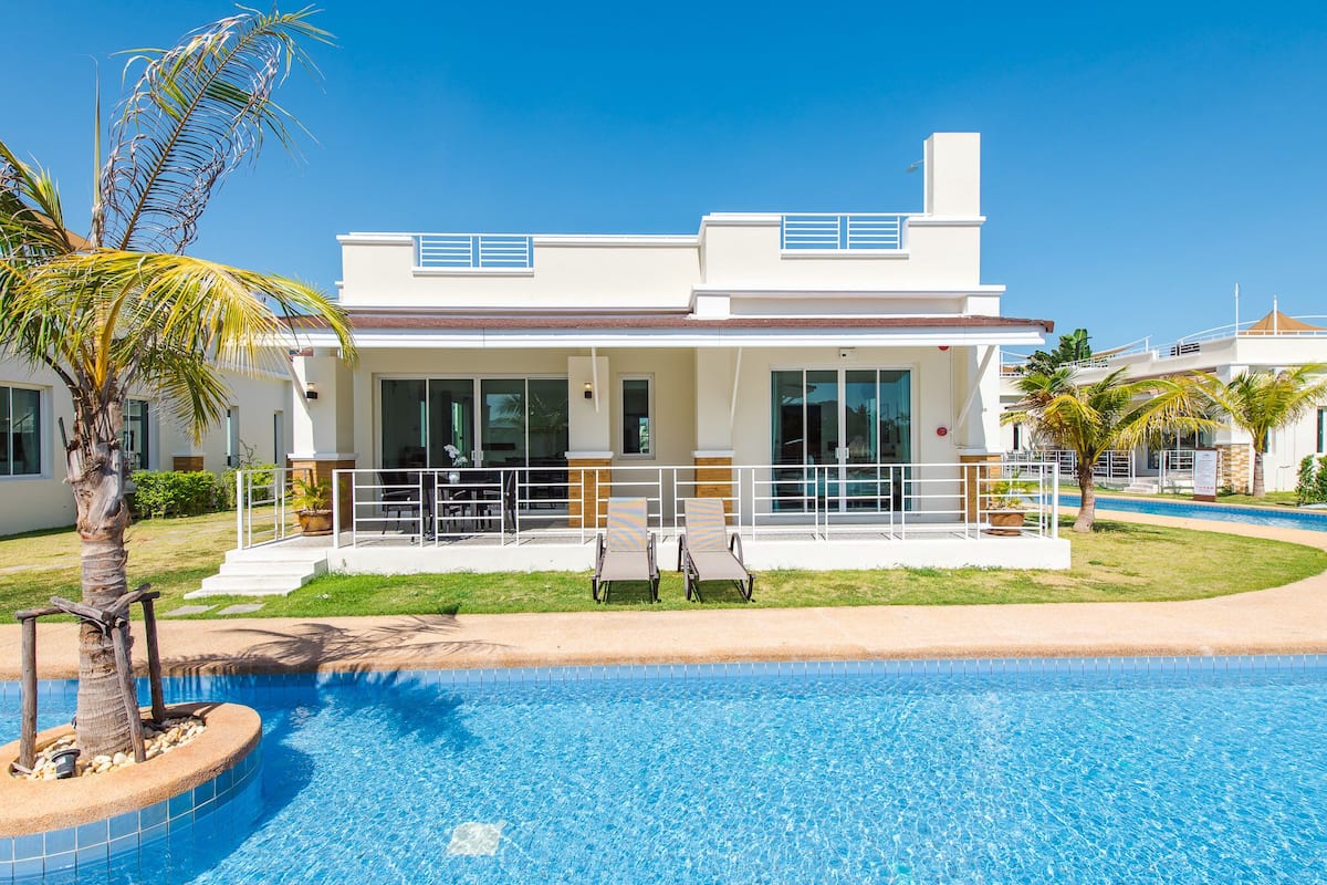 A modern hotel with a swimming pool, a covered patio, and a well-maintained lawn.